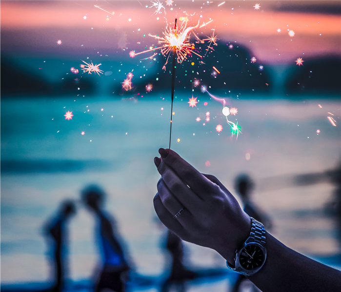 sparkler in a hand with people in the background with a pinkish sky